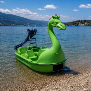 Bateau à pédales Grand Dragon vert avec toboggan vert, posé au bord de l’eau.